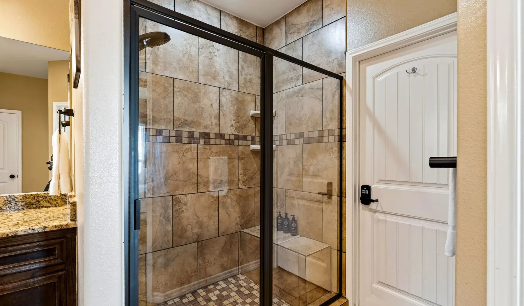 Un baño con azulejos, una ducha de vidrio y una puerta blanca.