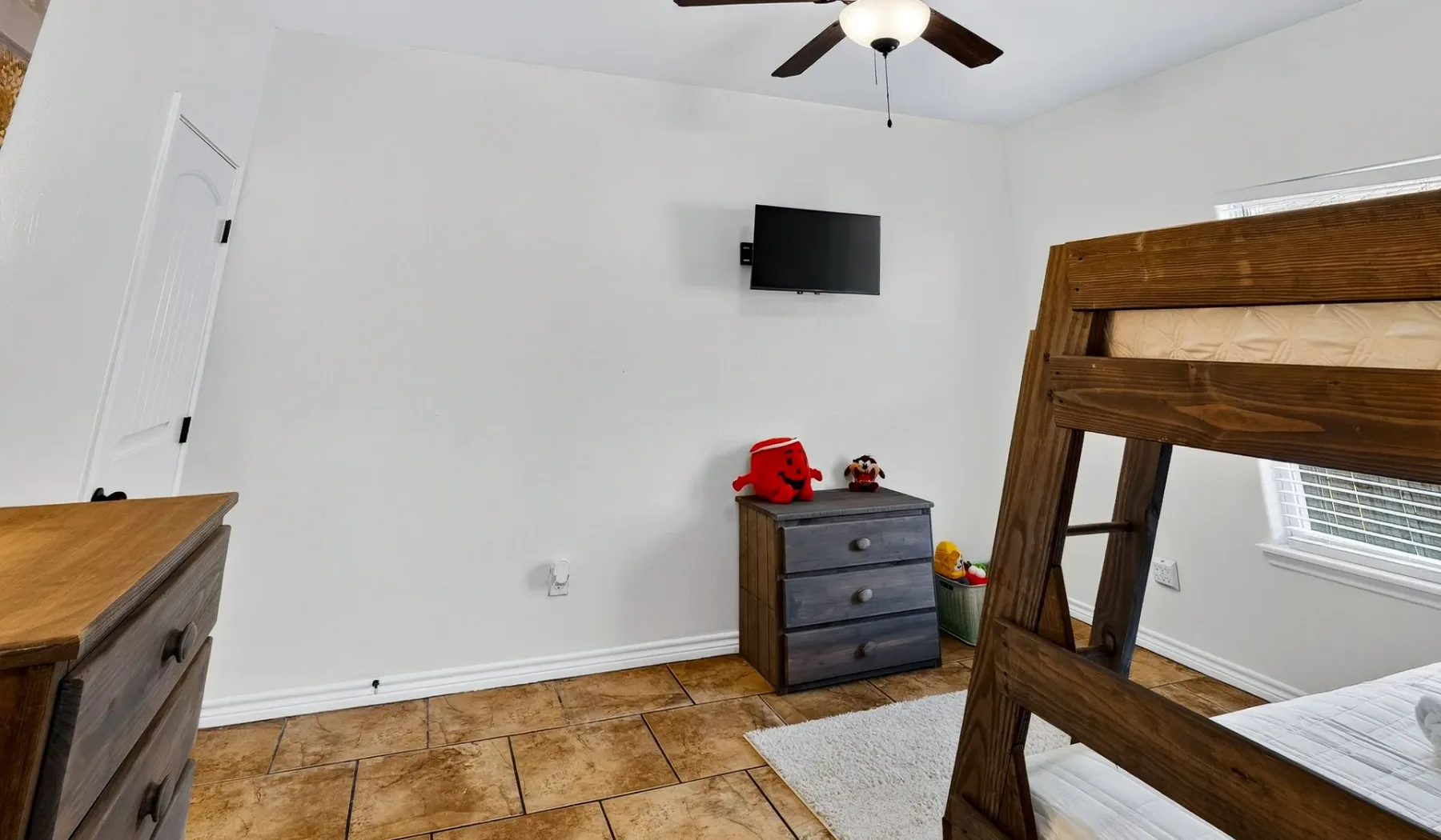 Dormitorio con una litera de madera, una cómoda y un televisor en la pared.