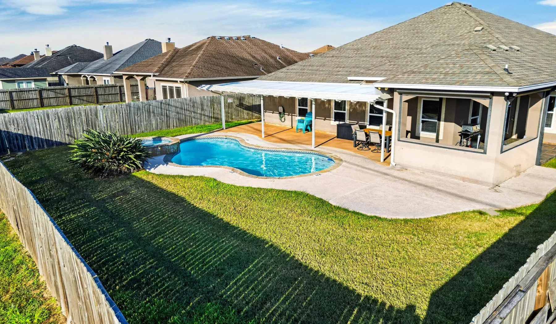 Un patio trasero cercado con piscina y terraza cubierta junto a la casa.