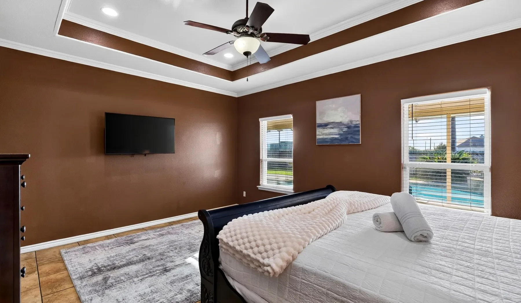 Un dormitorio con una cama grande, un televisor en la pared y ventanas con vista a una piscina.
