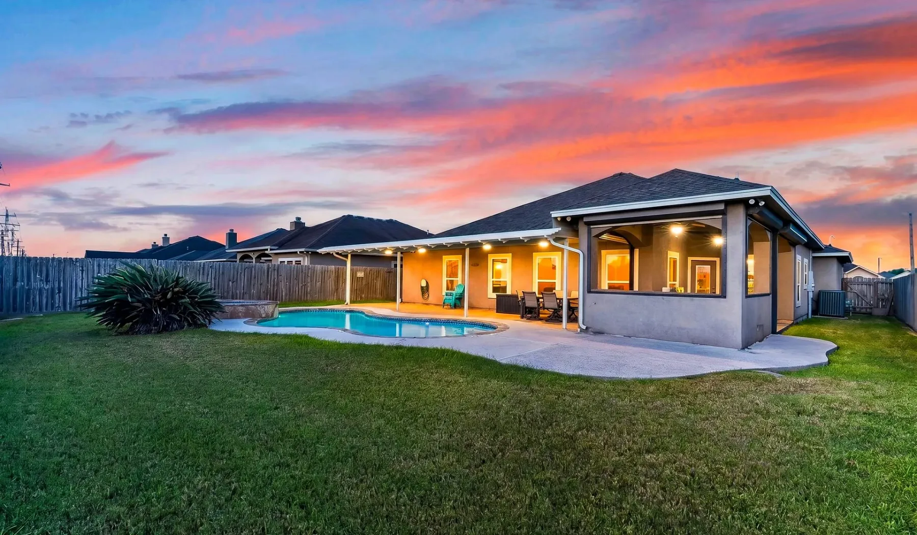 Una casa y una piscina en el patio aparecen bajo un cielo colorido al atardecer.
