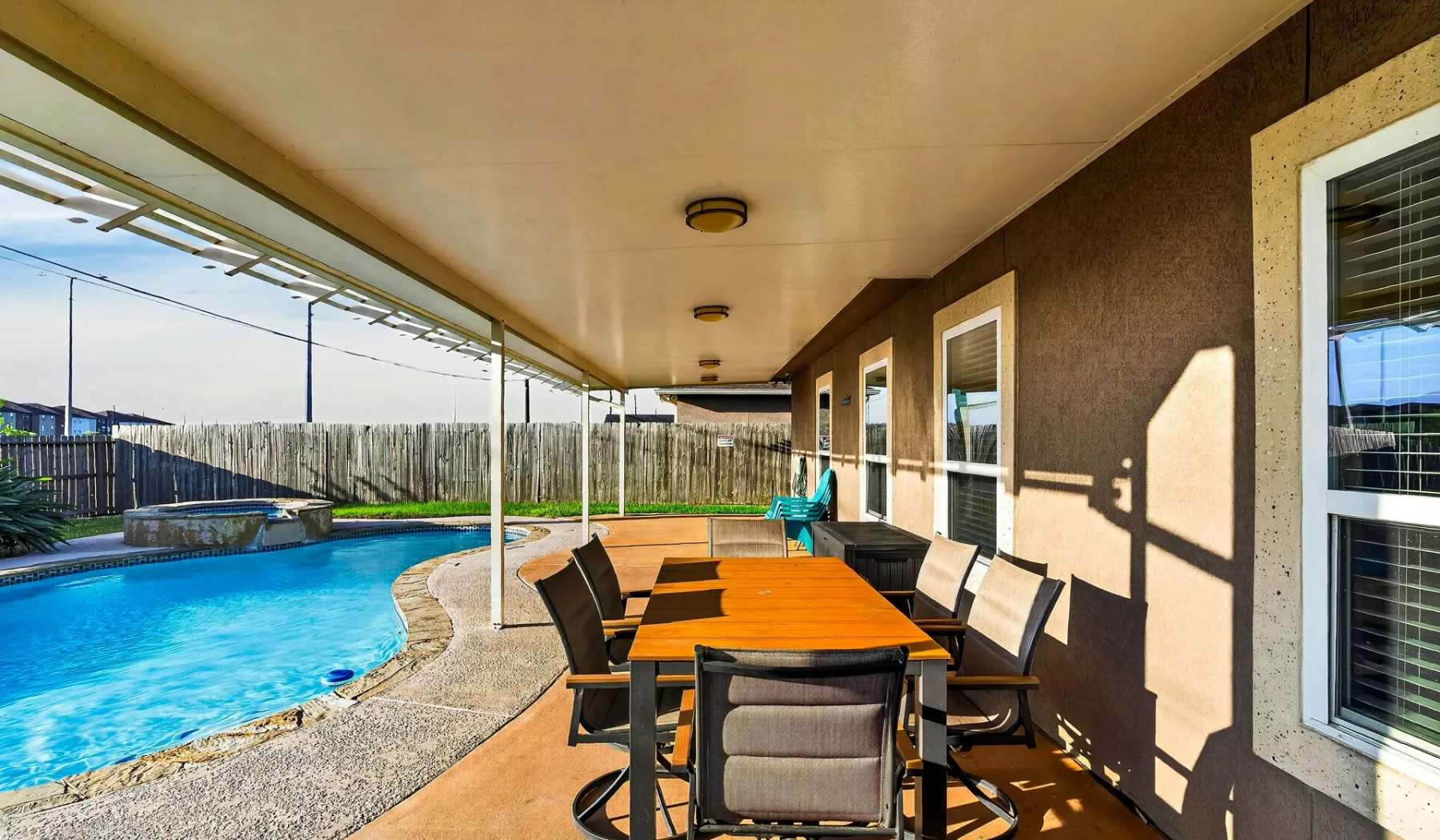Un patio cubierto tiene una mesa larga junto a una piscina.
