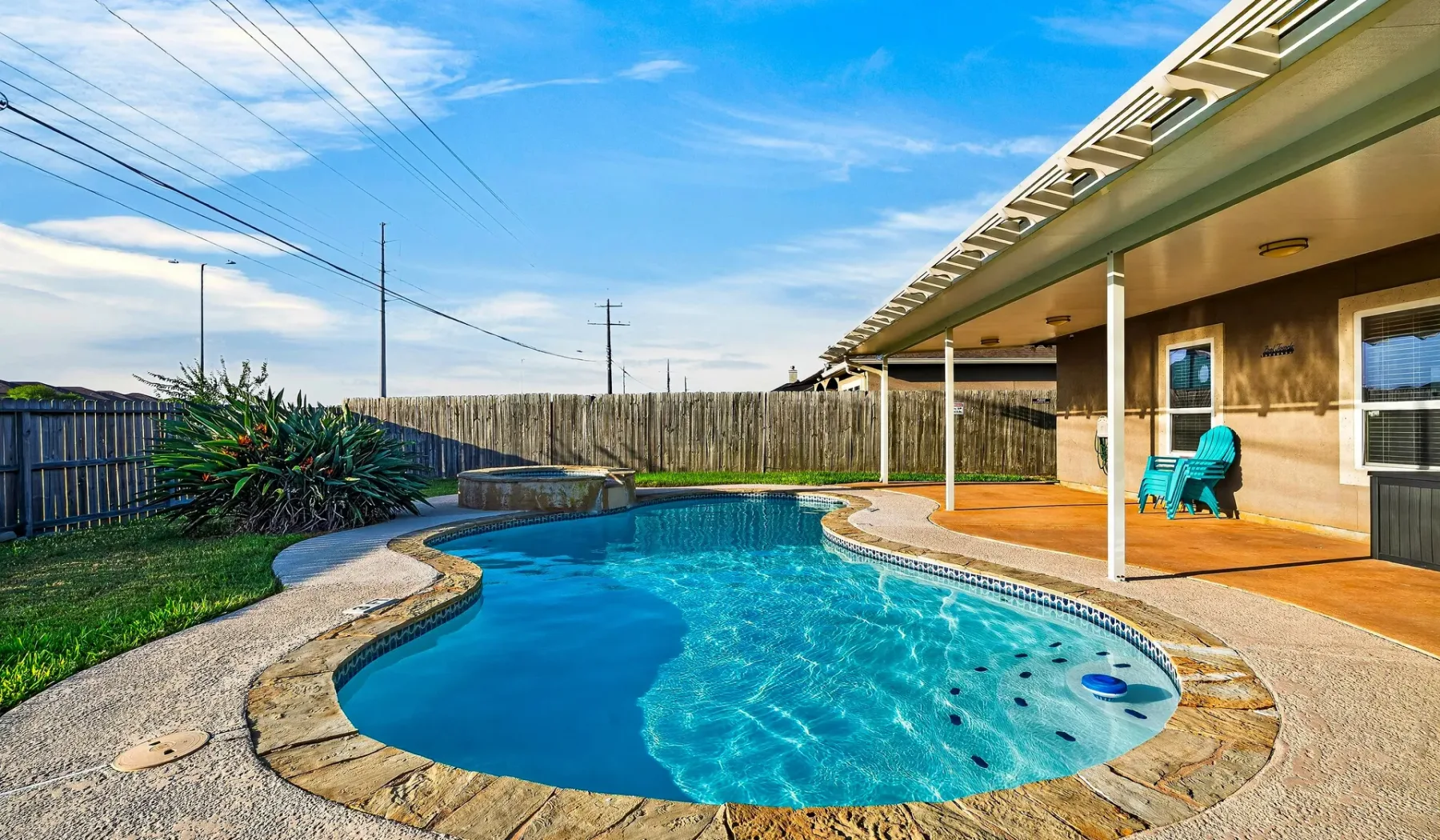Una piscina exterior curva está junto a un patio cubierto.