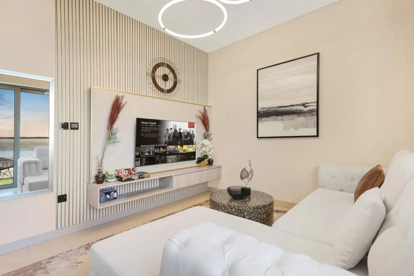 Una sala de estar con asientos blancos, un televisor montado en la pared y una mesa de centro redonda.
