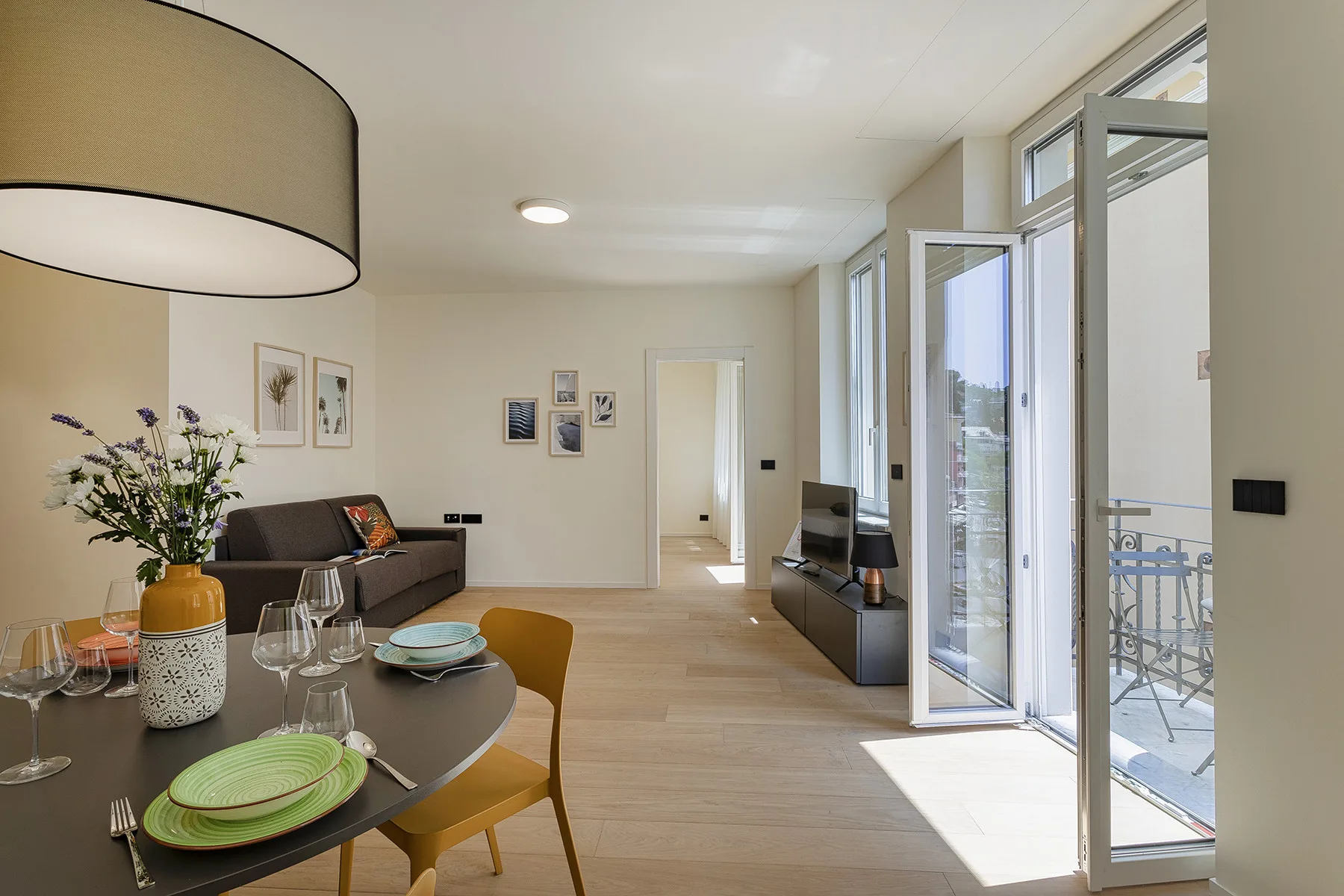 A bright dining and living area opens onto a balcony through tall glass doors.