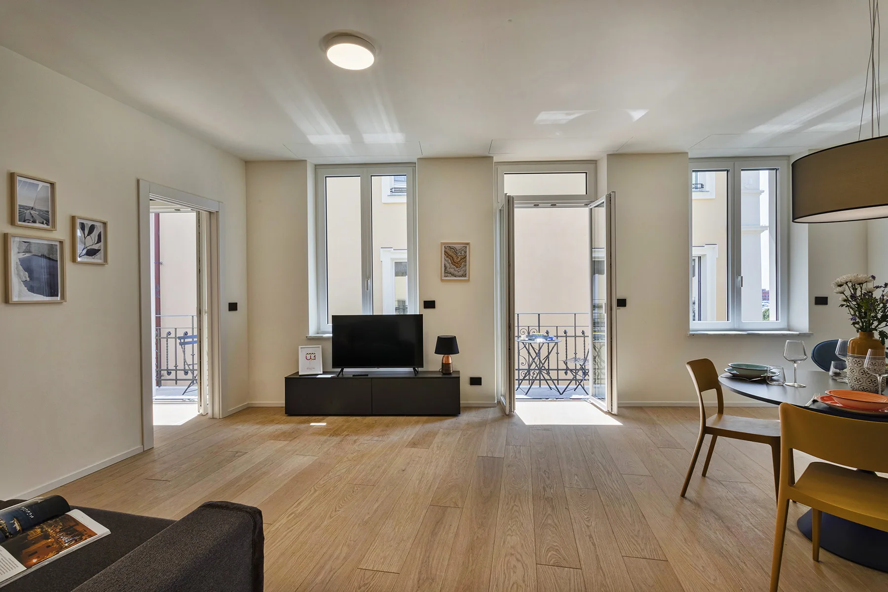 A bright living and dining area with large windows, a television, and a table.