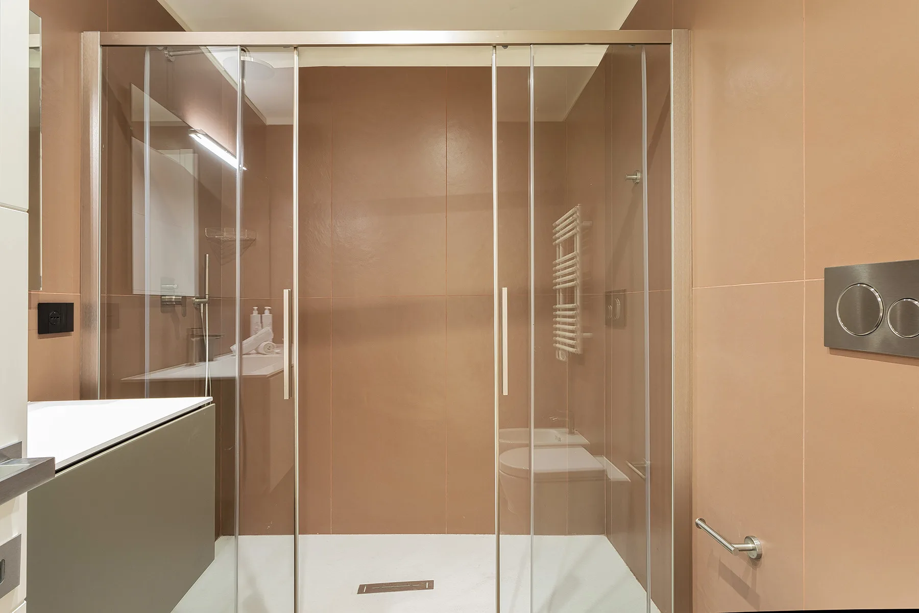 A bathroom shower with glass panels and beige tiled walls.