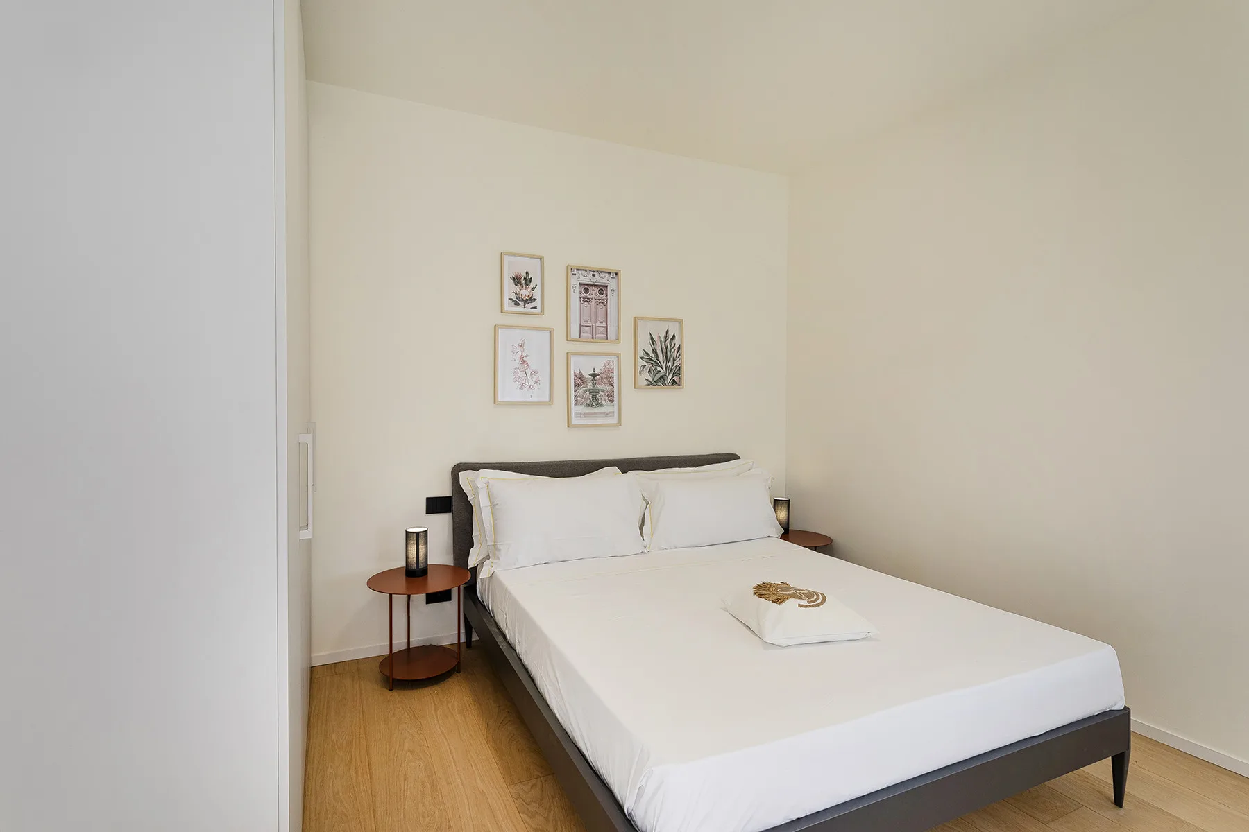 A bright bedroom with a neatly made bed and framed botanical prints.