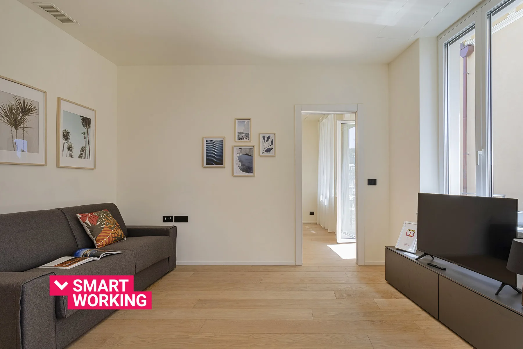 A bright living room with seating, framed wall art, and a television.