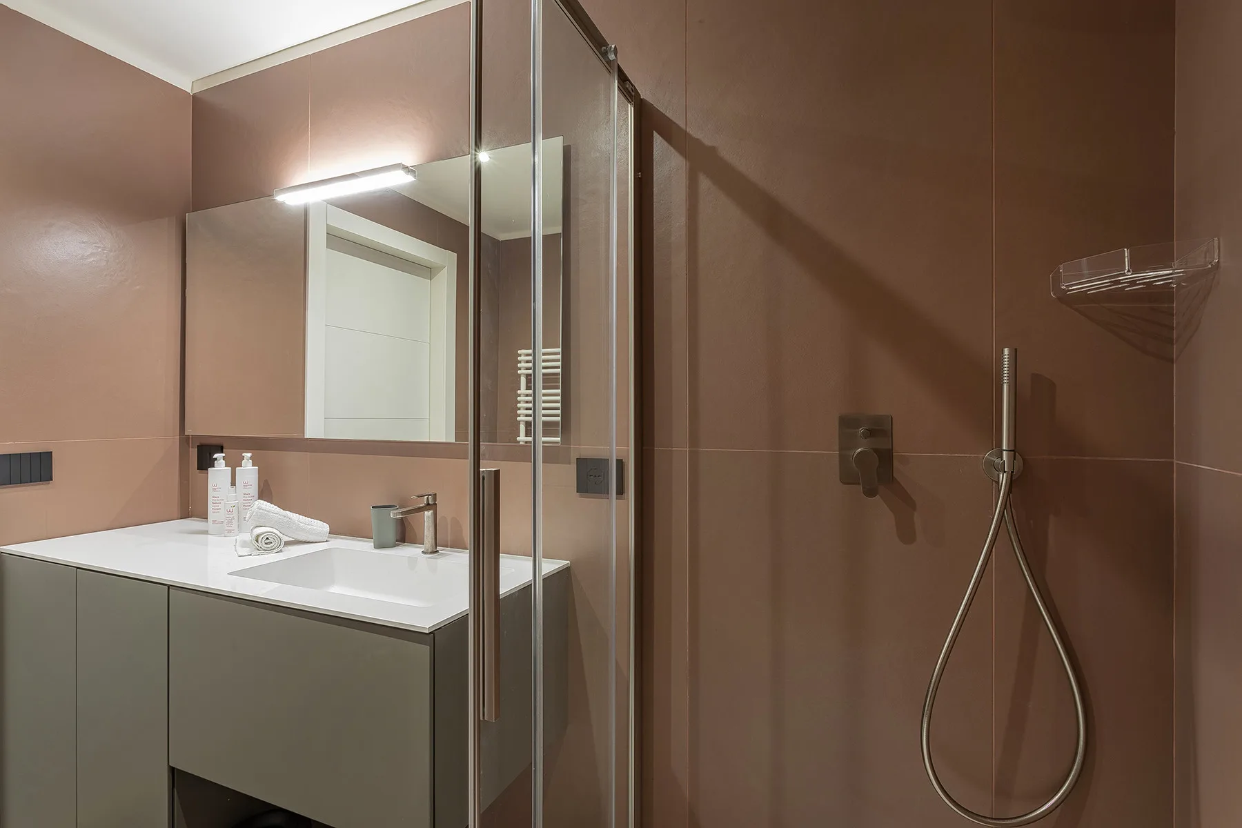 A bathroom with a vanity, mirror, and wall-mounted shower.