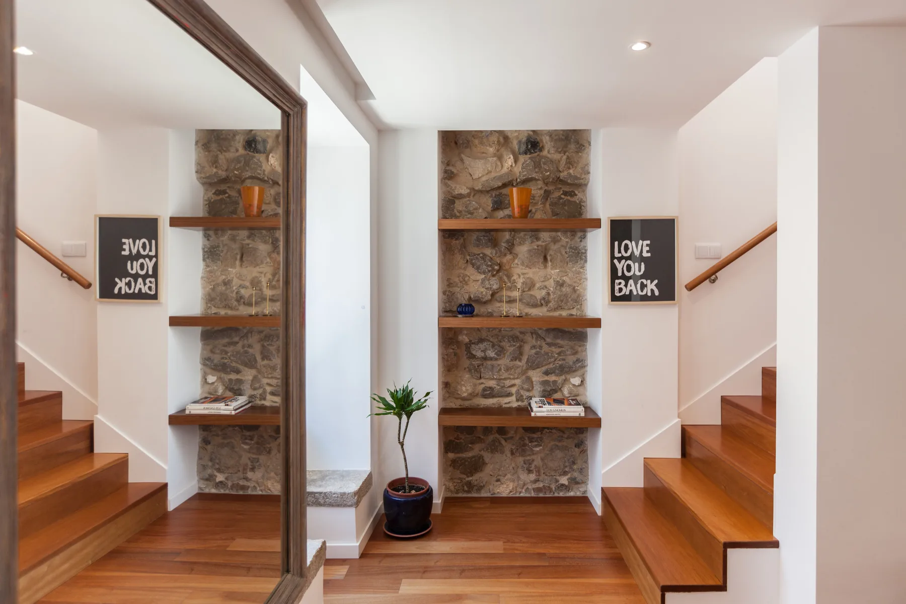 Una escalera luminosa con peldaños de madera y una estantería con fondo de piedra.