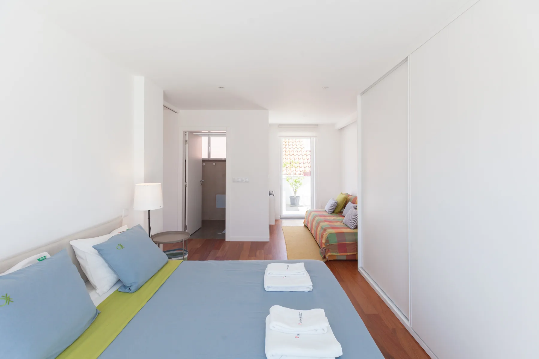 Un dormitorio con cama, ropa de cama colorida y una zona de estar junto a la ventana.