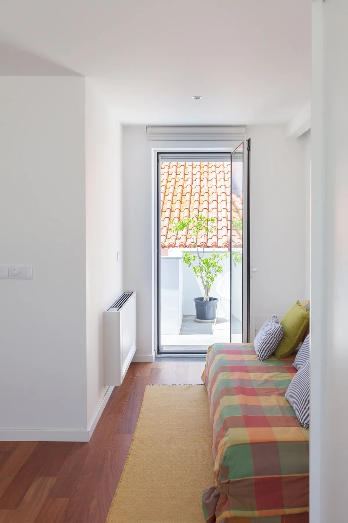 Una sala estrecha con asientos coloridos y una puerta de vidrio abierta hacia un pequeño espacio exterior.