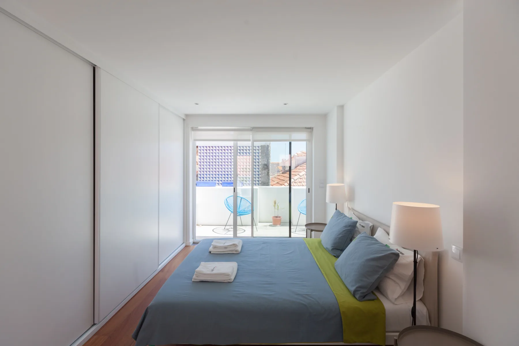 Dormitorio con una cama, lámparas de noche y puertas correderas de cristal que dan a un balcón.