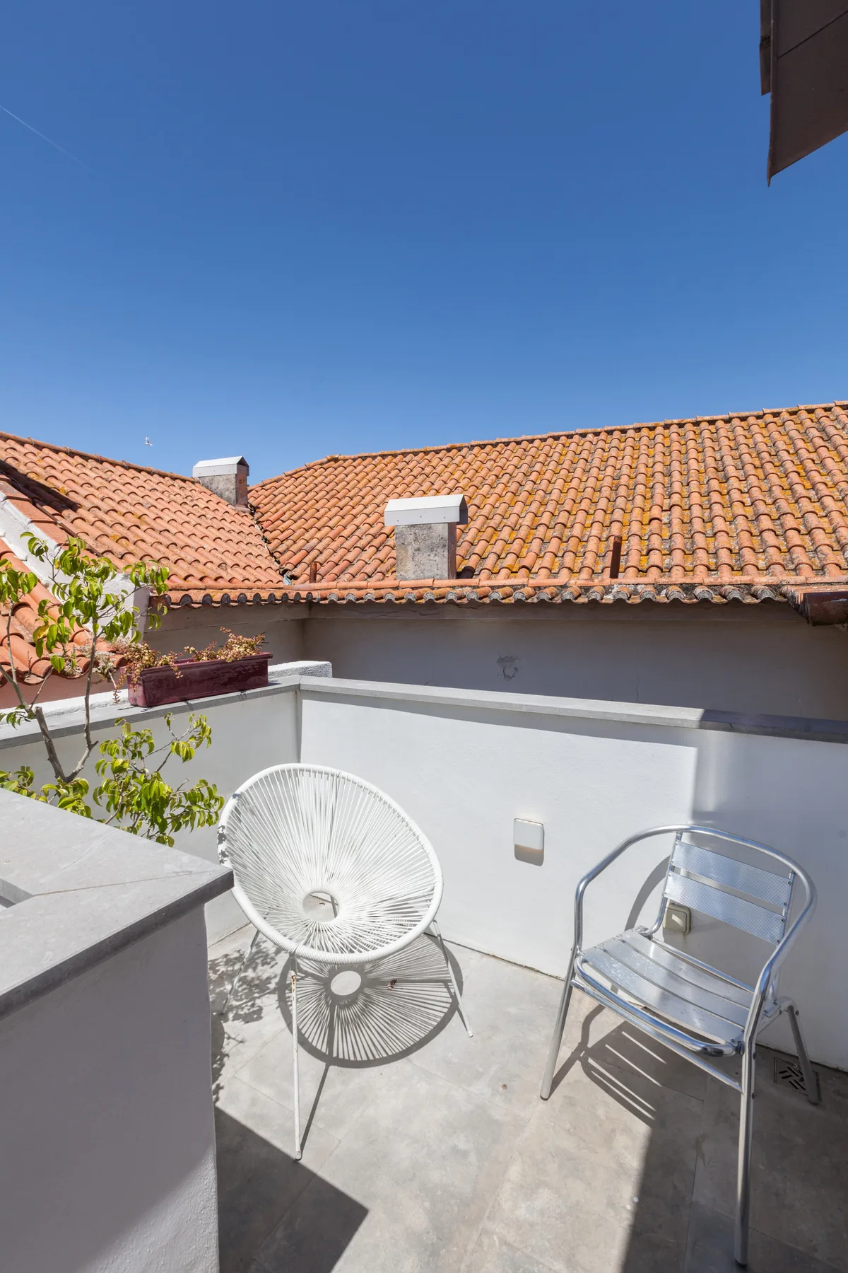 Una terraza soleada con dos sillas y tejados de tejas al otro lado del muro.
