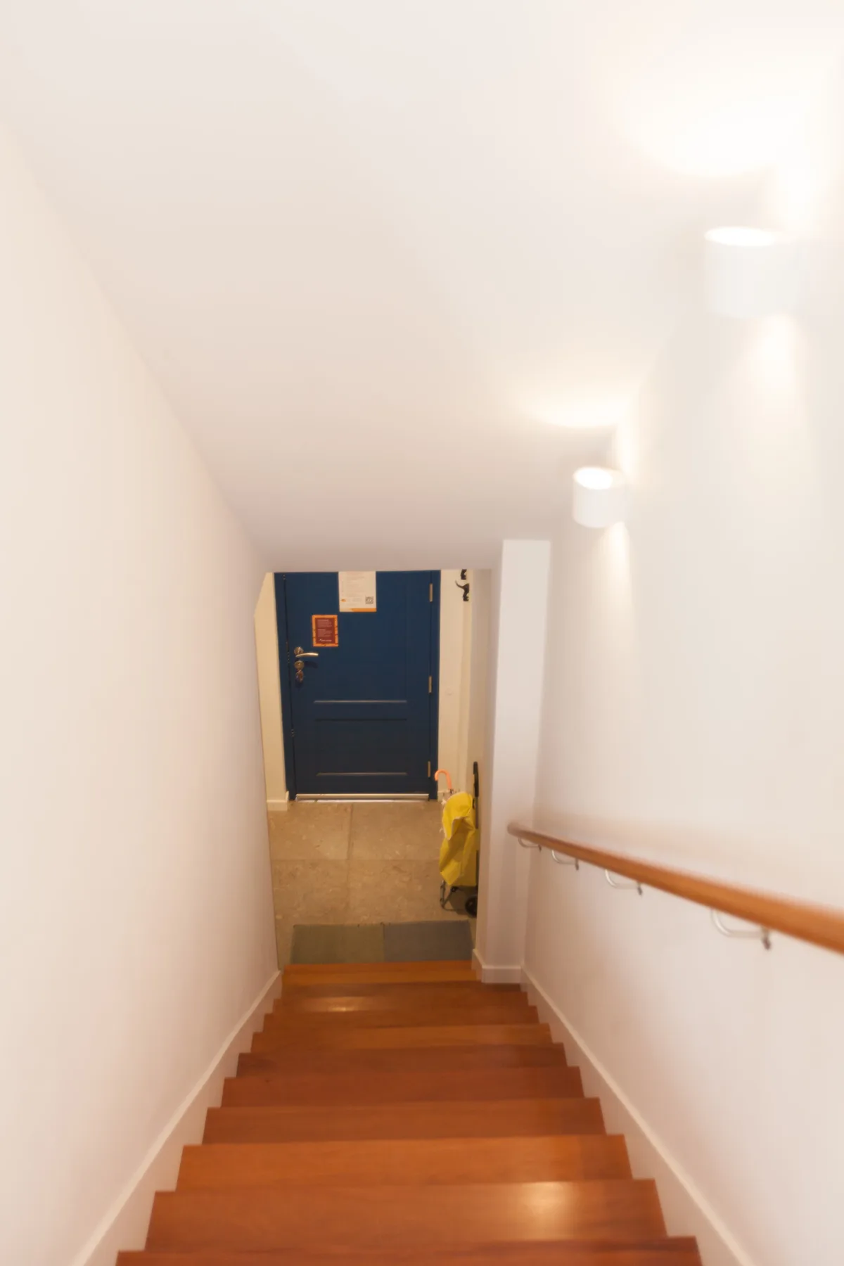 Una escalera interior luminosa baja hacia una puerta azul oscuro.