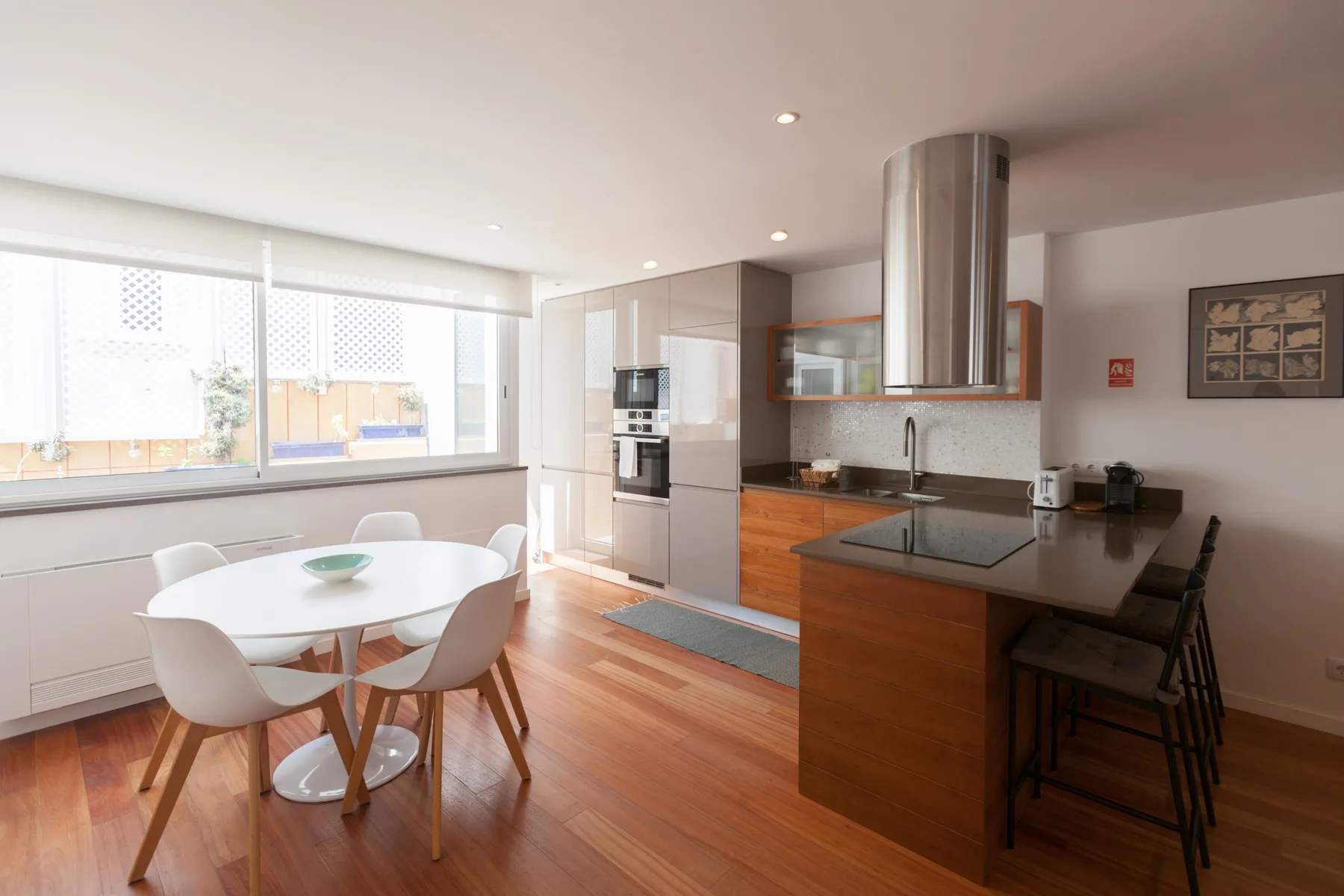 Una cocina y comedor luminosos con una barra y una mesa junto a grandes ventanas.