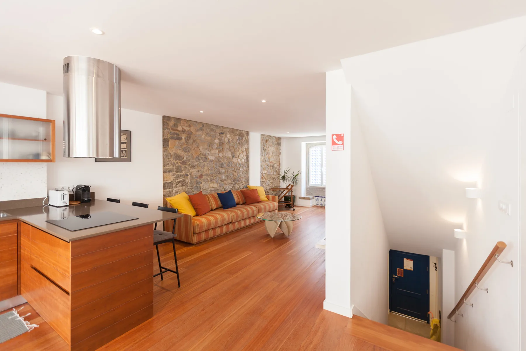 Sala de estar y cocina de concepto abierto, con un sofá junto a una pared de piedra.