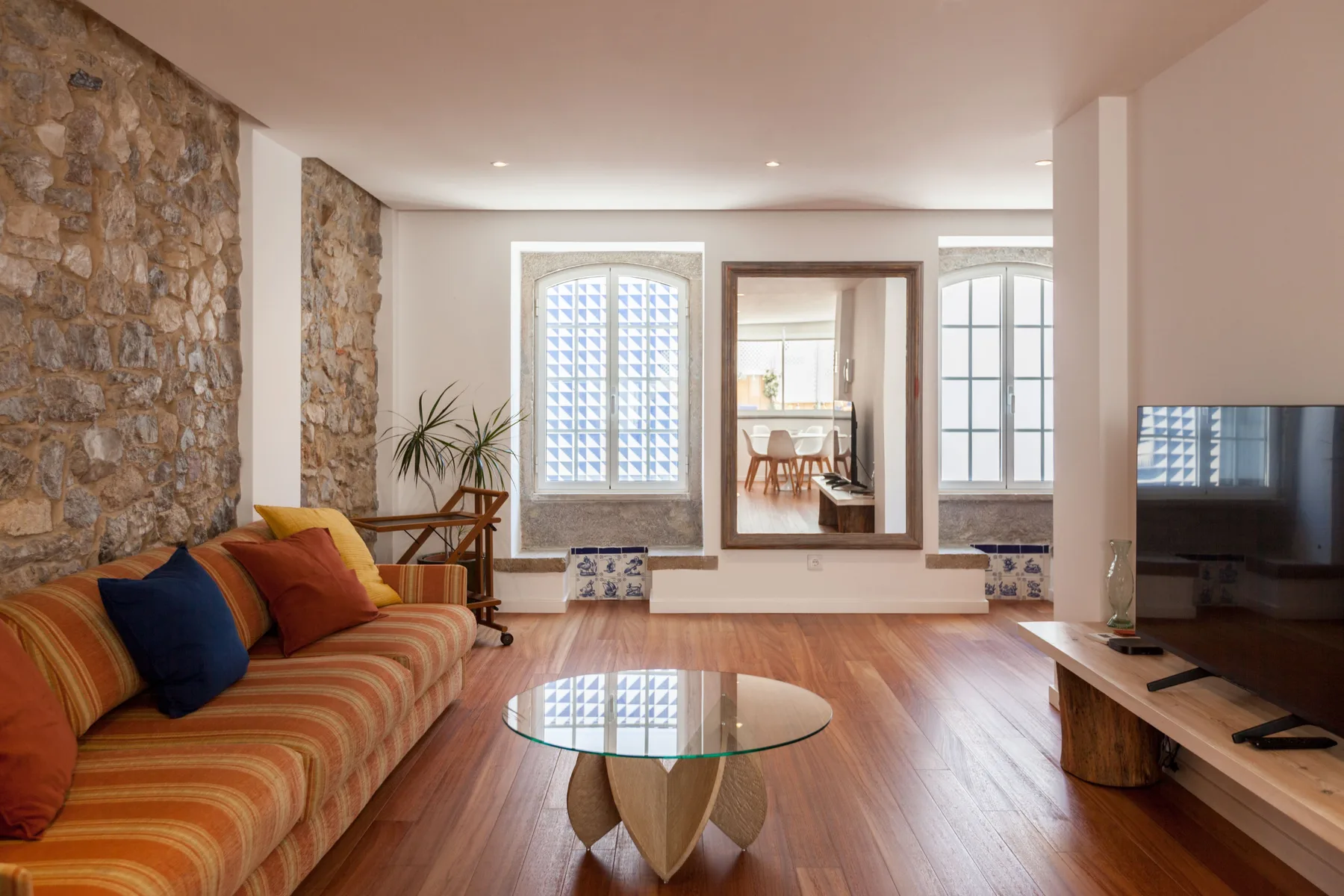 Sala de estar con asientos a rayas, una mesa de centro de vidrio y paredes de piedra.