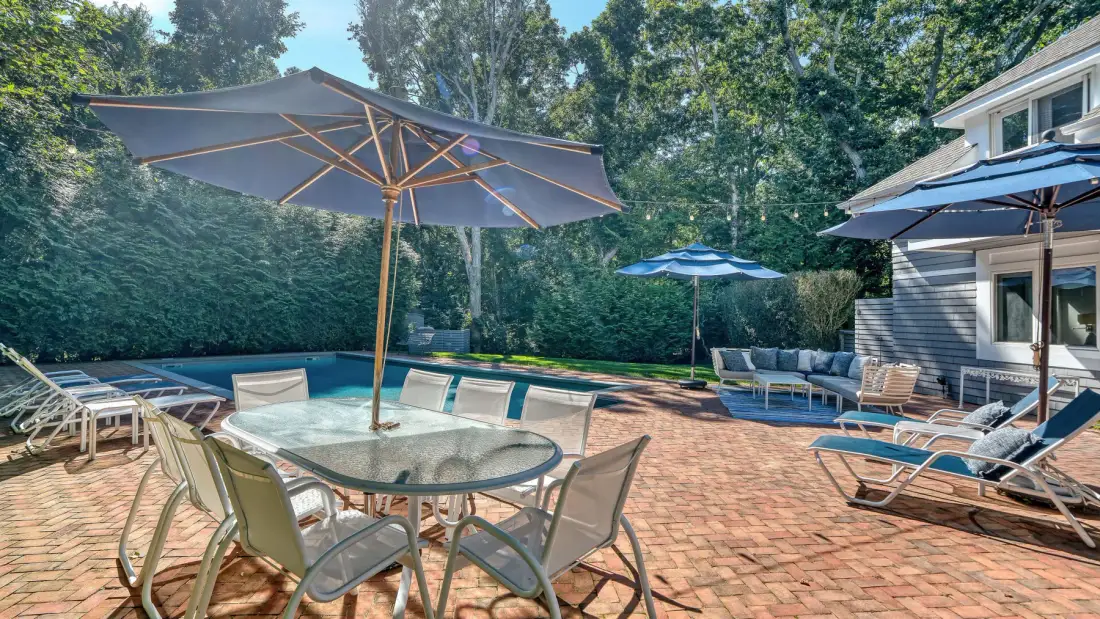 Un patio de ladrillo con asientos y sombrillas junto a una piscina.