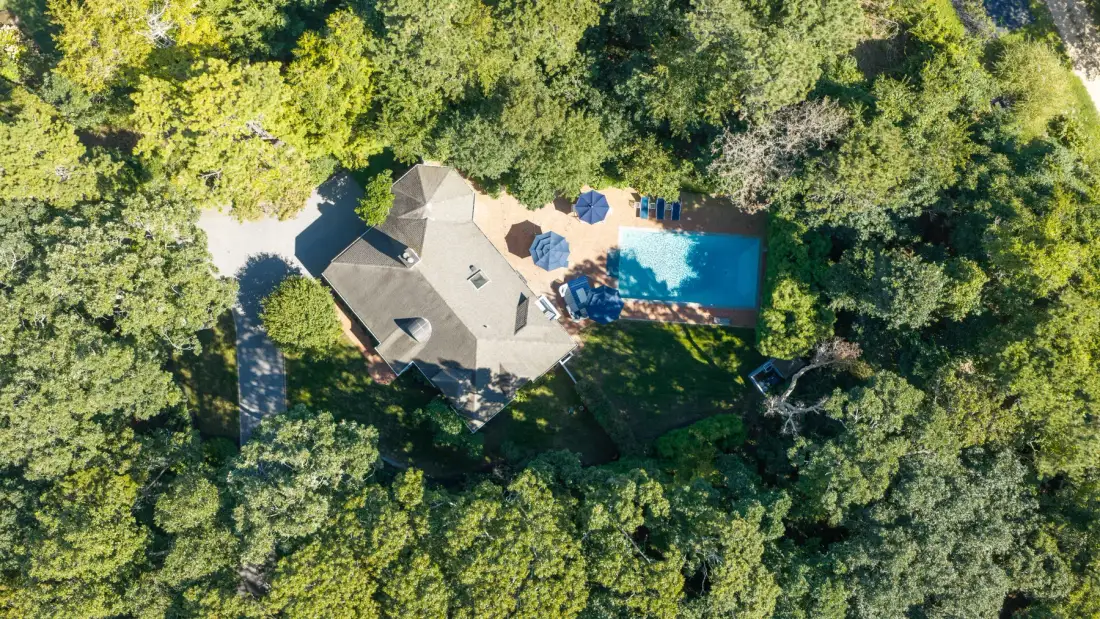 Una vista aérea muestra una casa y una piscina rodeadas de árboles.