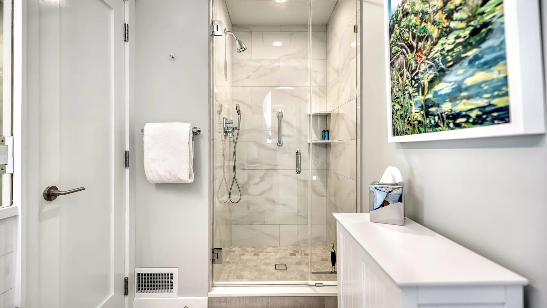 Un baño luminoso con una ducha de cristal y un largo lavabo blanco.