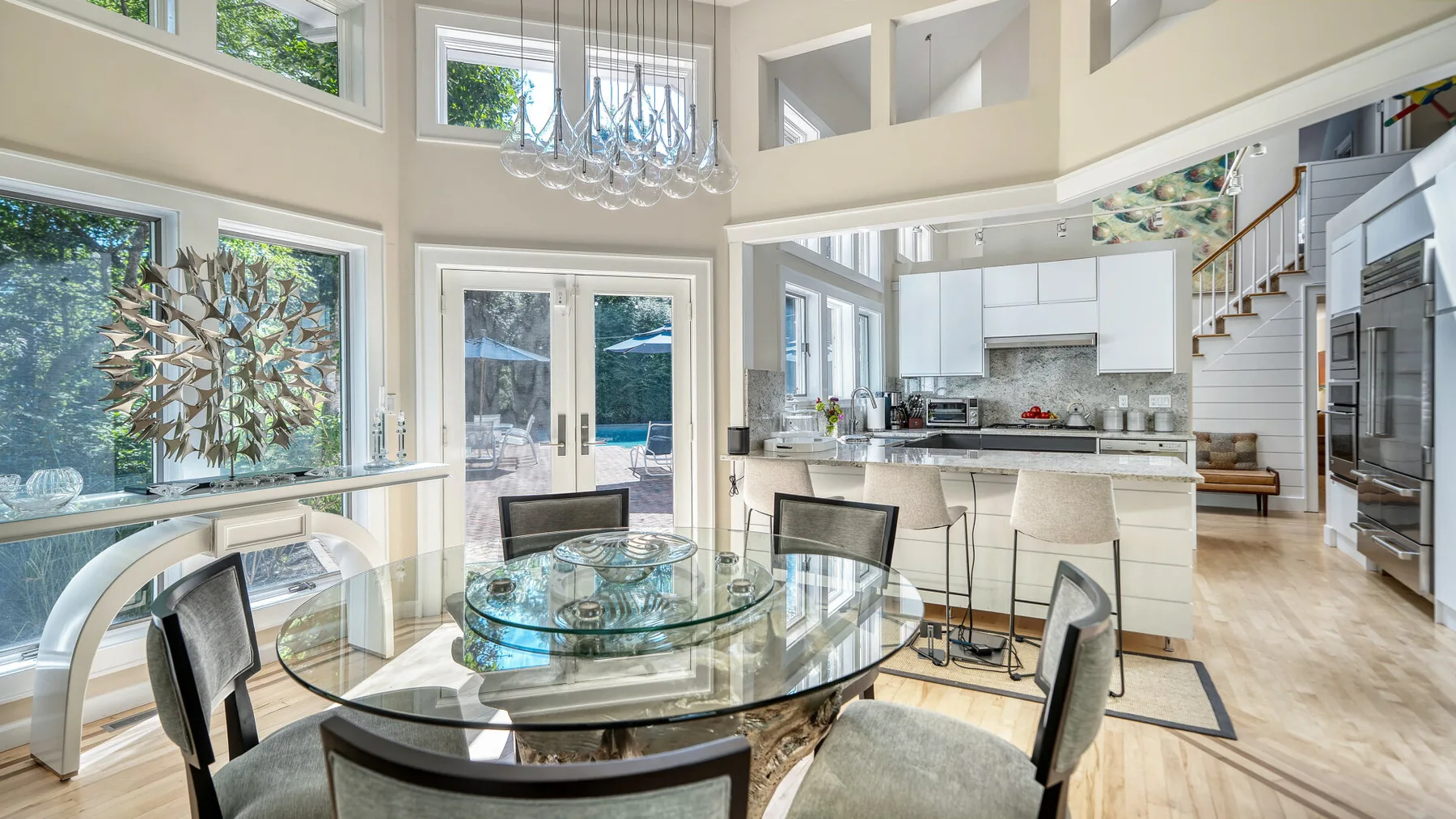 Un comedor y cocina diáfanos y luminosos, con grandes ventanas y una mesa de vidrio.