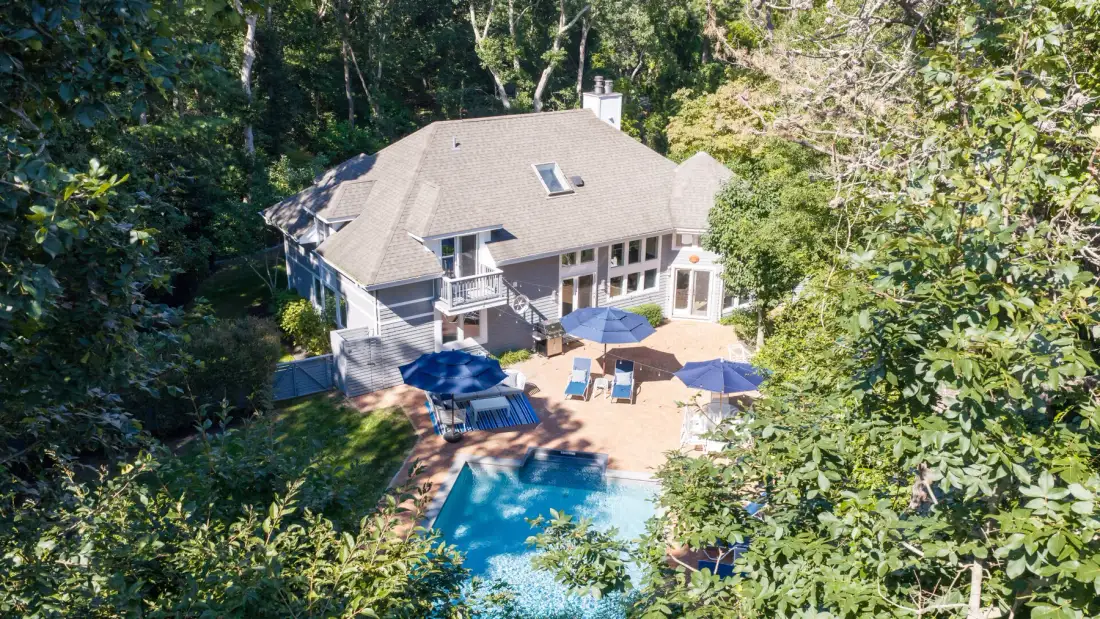 Una casa rodeada de árboles tiene una piscina y un patio.