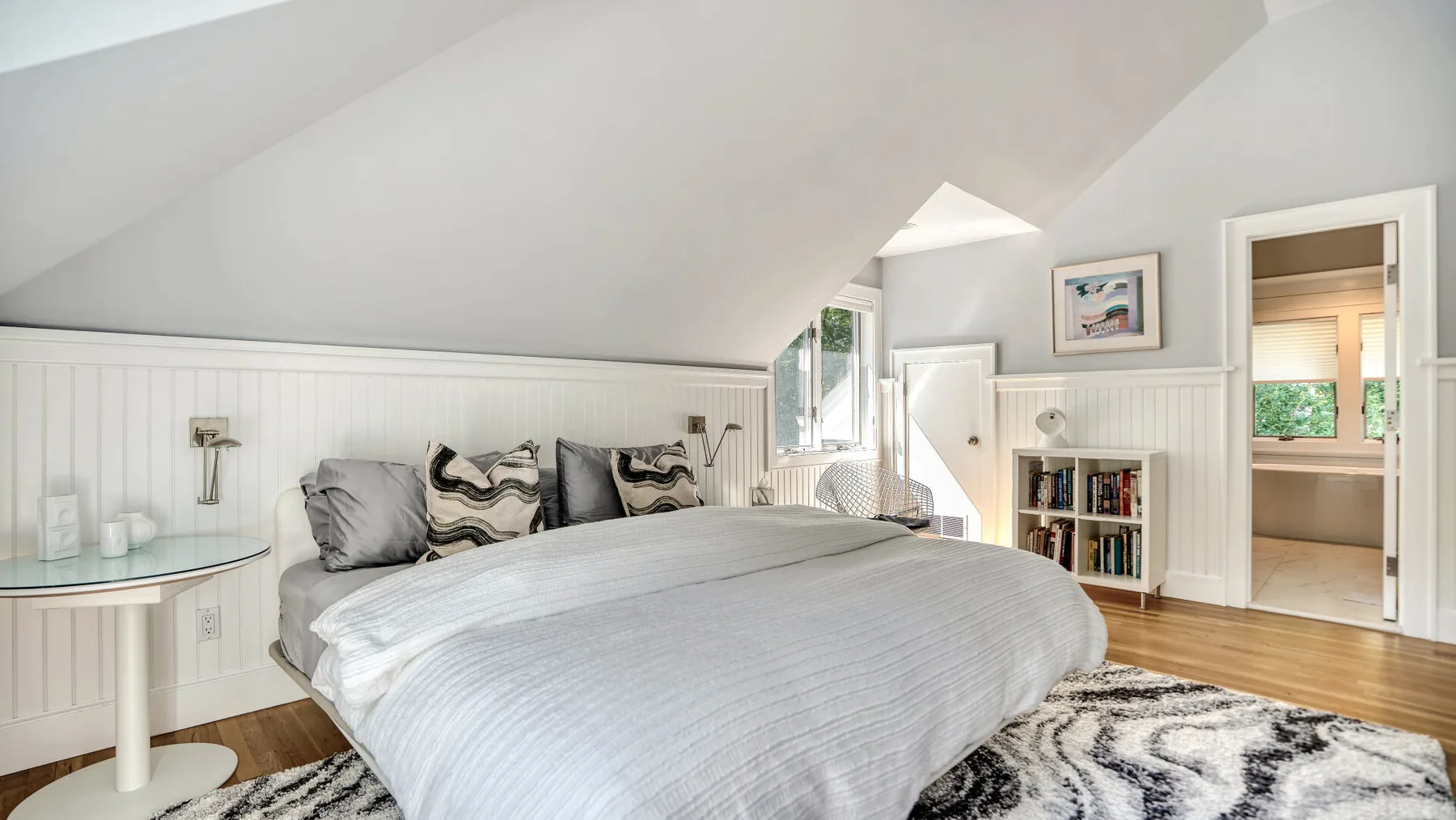 Un dormitorio abuhardillado luminoso con una cama bajo un techo inclinado.