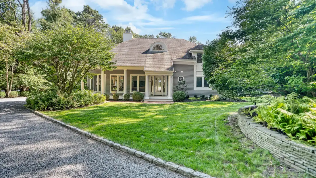 Una casa junto a una entrada curva, con césped verde y árboles.