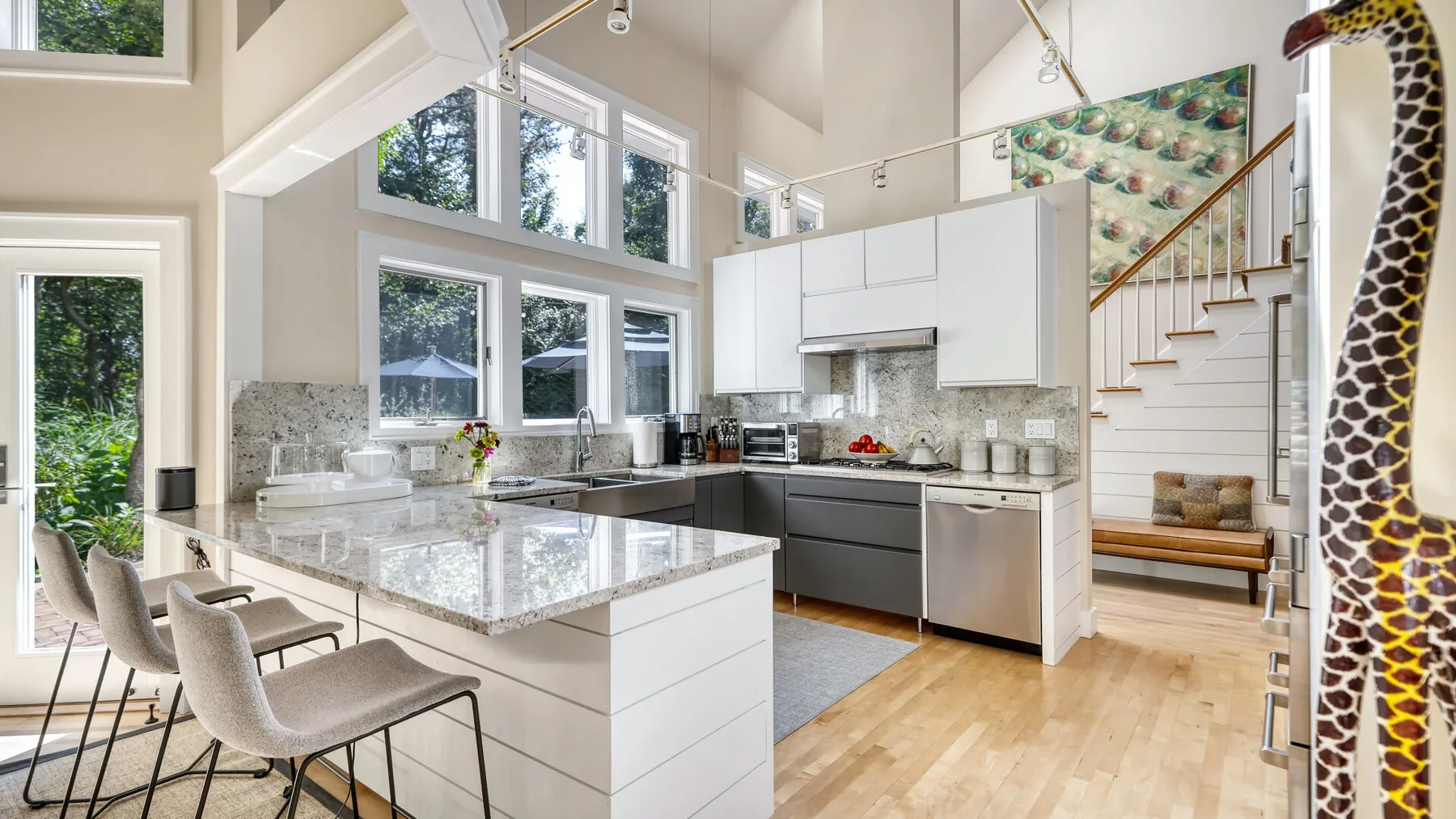 Una cocina diáfana y luminosa con una isla grande, ventanas y una escalera.