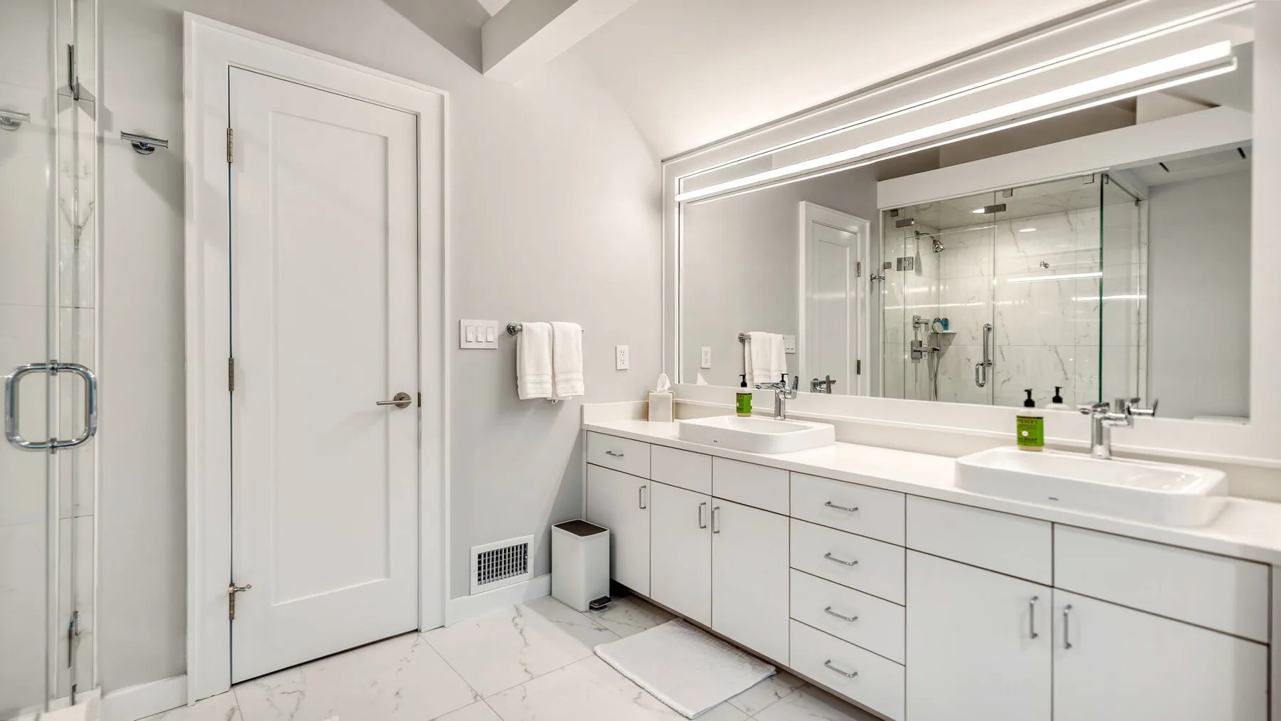 Un baño luminoso con un tocador largo, lavabos y una ducha de vidrio.