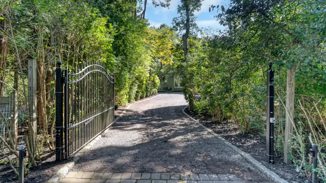 Un camino pavimentado atraviesa una puerta abierta entre árboles y arbustos frondosos.