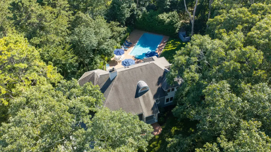 Vista aérea de una casa rodeada de árboles, con una piscina cerca.