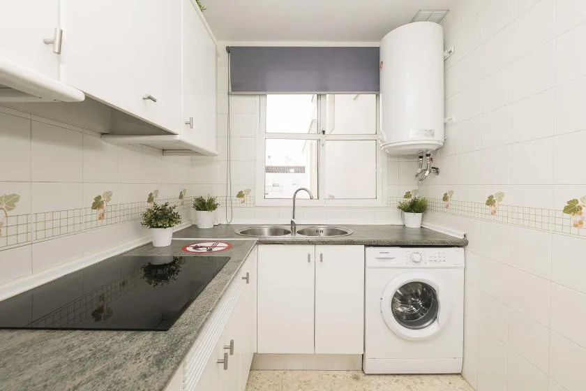A bright kitchen with a countertop, sink, and washing machine.