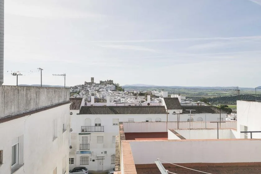 A rooftop view overlooks white buildings and a distant town beneath a bright sky.