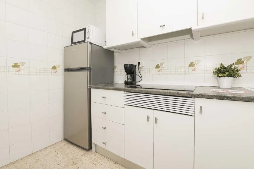A tiled kitchen with white cabinets, a refrigerator, and a countertop.
