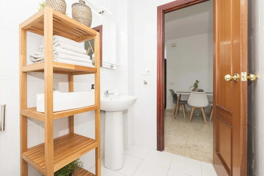 A bright bathroom with a wooden shelving unit holding folded towels beside the sink.