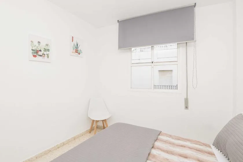 A bright bedroom with a bed, wall art, and a window with a lowered blind.