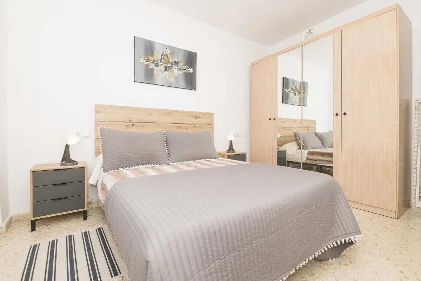 A bright bedroom with a neatly made bed and a mirrored wardrobe.