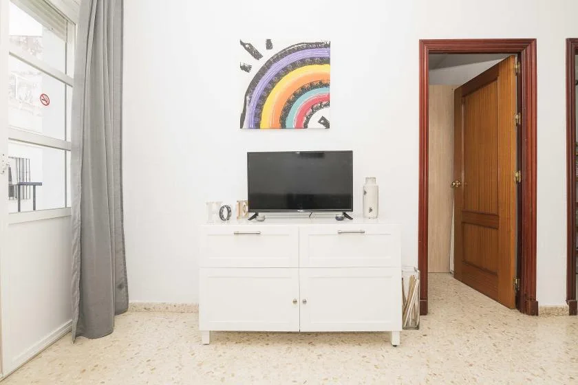 A bright room with a television on a white cabinet beneath a colorful rainbow painting.