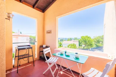 Una terraza luminosa con una mesa pequeña y asientos junto a grandes ventanas abiertas.