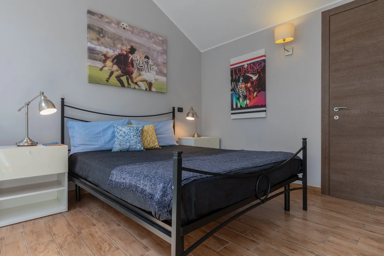 A bedroom with a black bed, colorful wall art, and a wooden door.