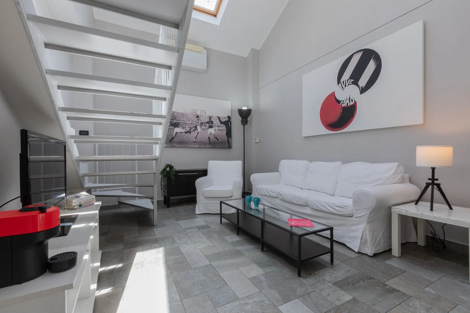 Una sala luminosa con asientos blancos, una mesa de centro de vidrio y una escalera.