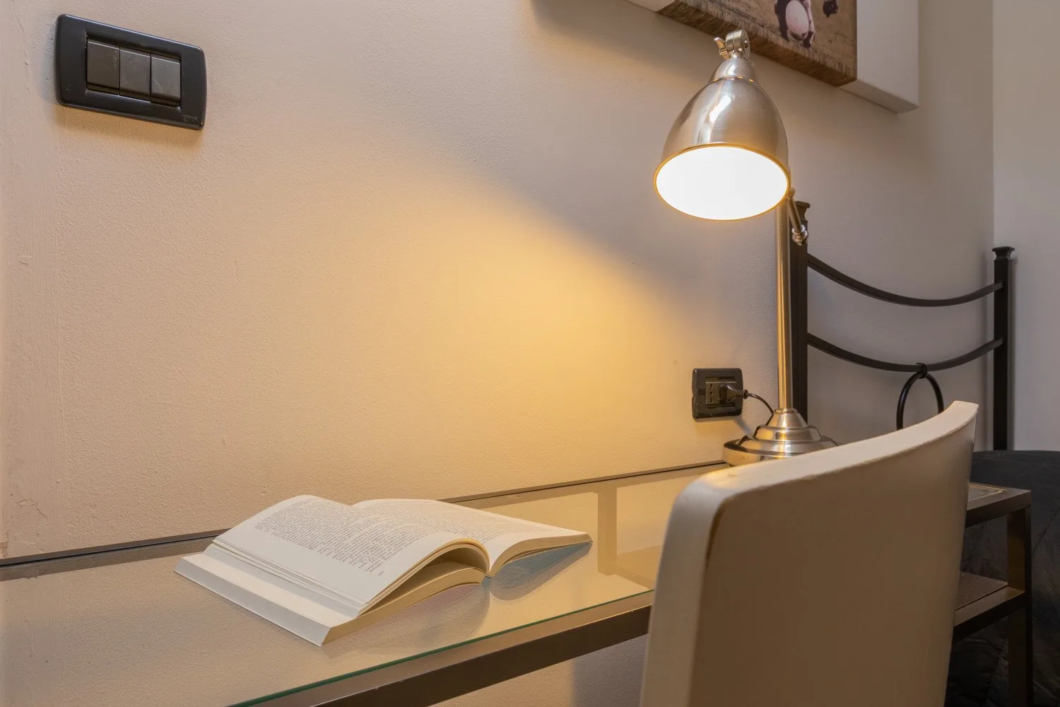 Un escritorio de estudio con un libro abierto bajo una lámpara encendida.