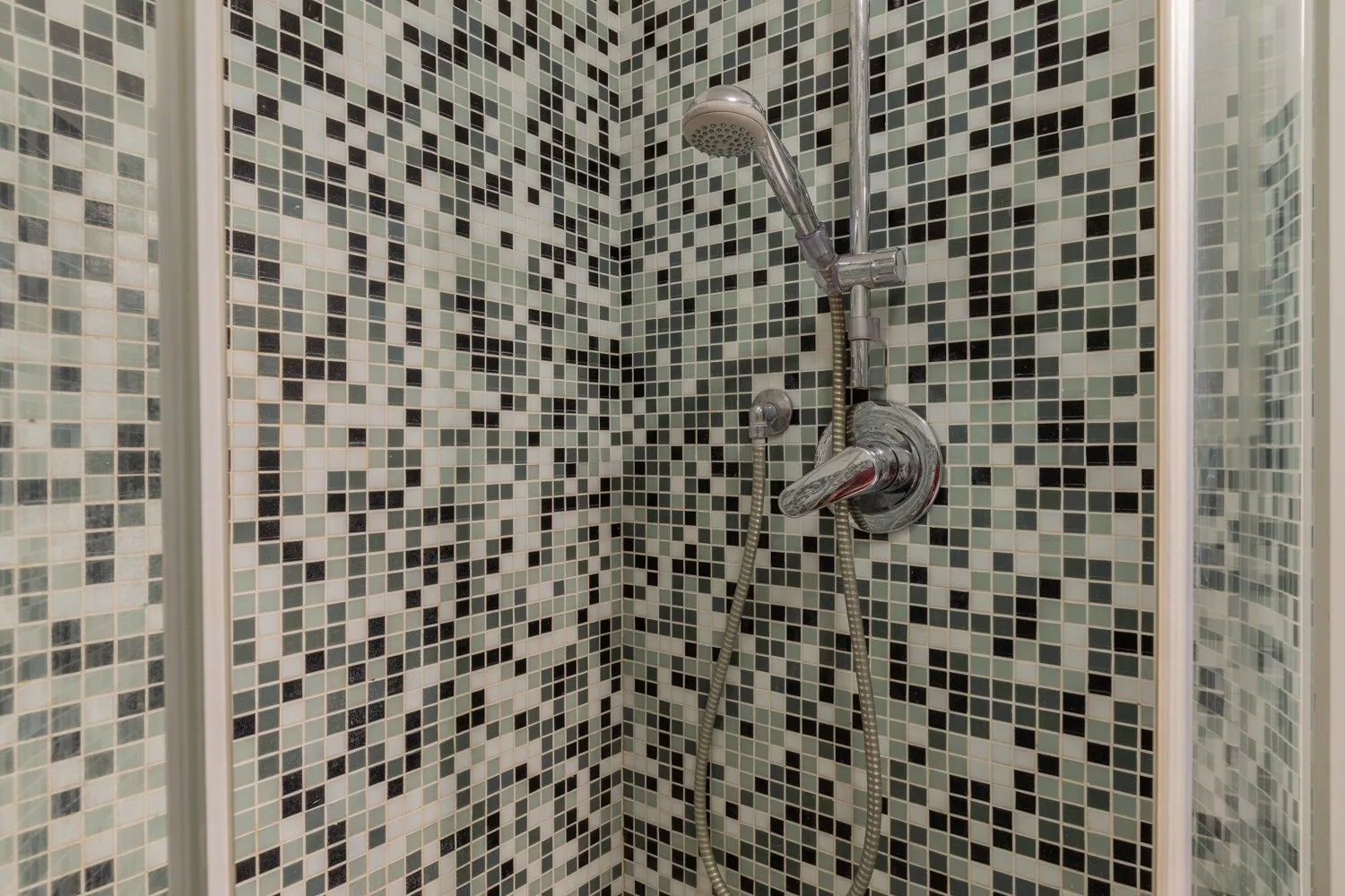 Una ducha con azulejos, una ducha de mano y controles en la pared.