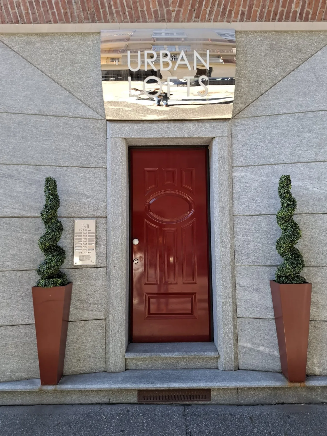 Una puerta roja está integrada en una fachada de piedra, flanqueada por plantas en macetas.