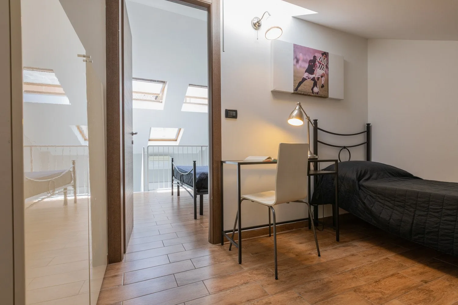 A bedroom with a bed, desk, and chair beside a bright adjoining area.