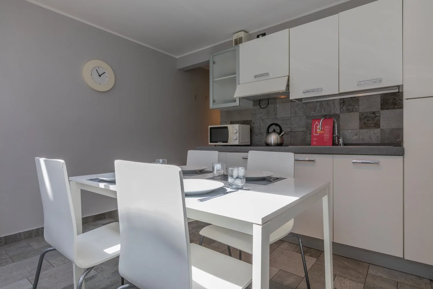 Un comedor con una mesa blanca y sillas junto a una cocina compacta.