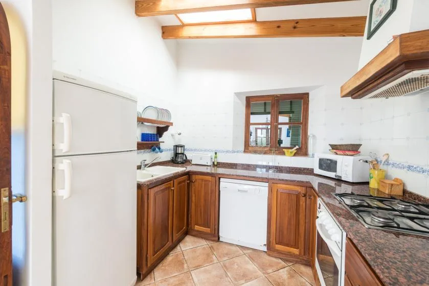 A bright kitchen with wooden cabinets, a refrigerator, and a window above the counter.